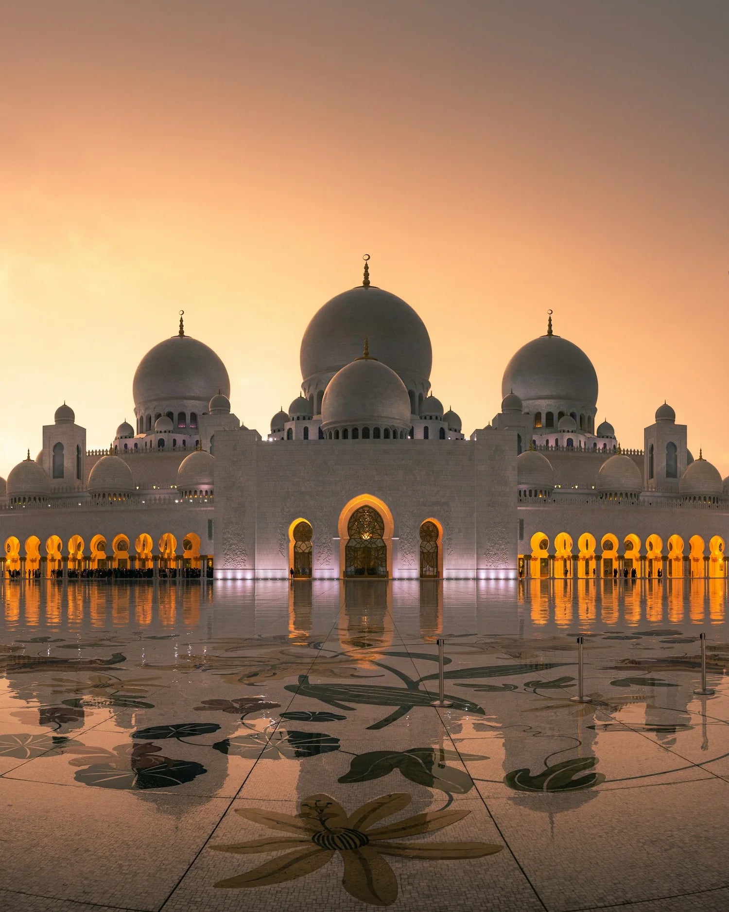 Grosse Moschee im Abendlicht — weisse Kuppeln, goldene Arkaden und ihr Spiegelbild im Wasser